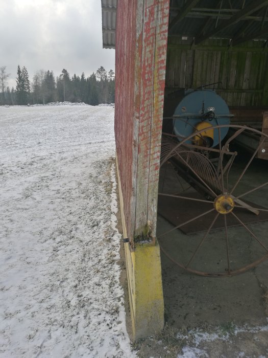 Öppet garage med synlig spricka i fundamentet, gammal maskin inne, snötäckt mark utanför.