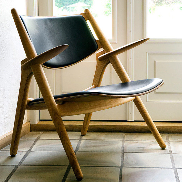 Designerfåtölj CH28 i trä med svart sits och ryggstöd, elegant i minimalistisk inredning.