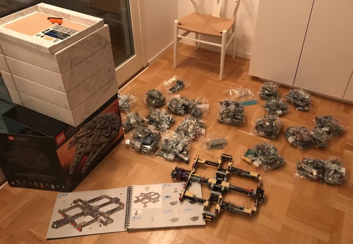 Starten av ett LEGO Star Wars byggprojekt på ett trägolv med sorterade påsar av bitar och instruktionsbok öppen.