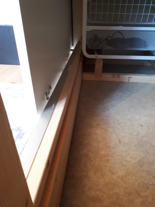 Stålprofil monterad på träregel längs med golvet, ingen dörrhjul synlig, med fokus på fästbeslag.