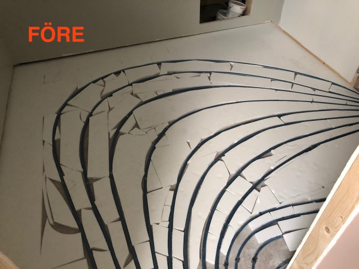 Slarvigt lagt golvvärmerör i en kurvig väg över en klädkammares golv med synliga skarvar och brutna isoleringsskivor.