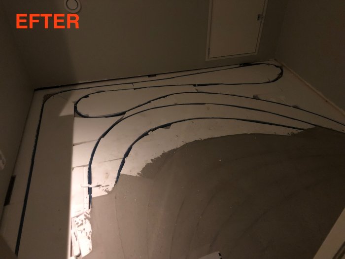 Ojämnt skarvat golvvärmerör längs ett betonggolv i en klädkammare markerat med "EFTER".