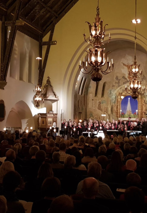 Kör framför publik i kyrksal med ljuskronor och väggmålningar.