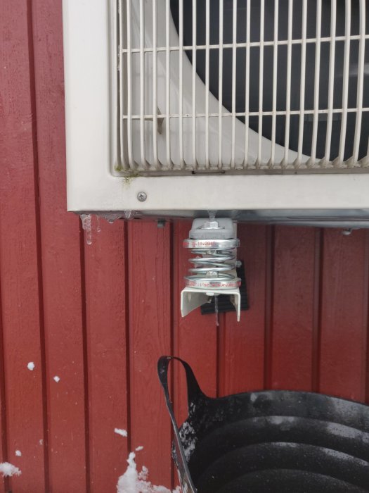 Utedel av värmepump monterad på röd trävägg med fjädrar och dämparmattor installerade.