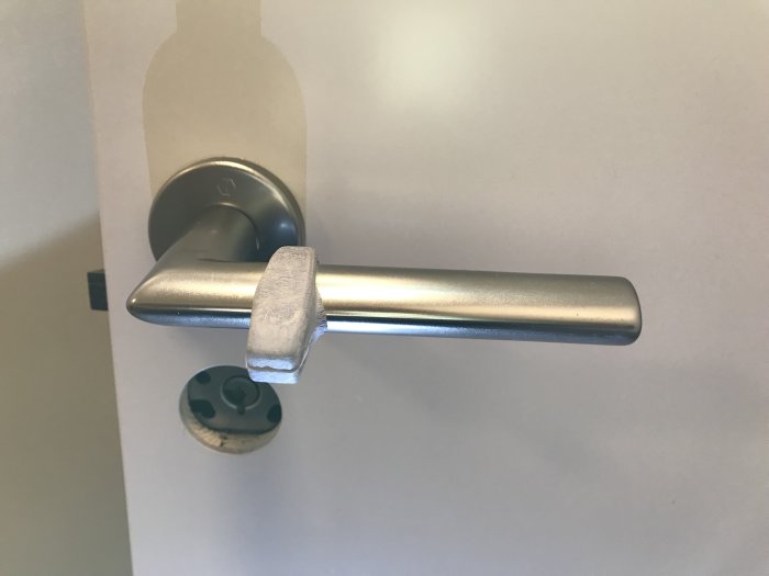 Närbild på en silverfärgad innerdörrshandtag utan synliga skruvar och ett litet hål vid foten av handtaget.