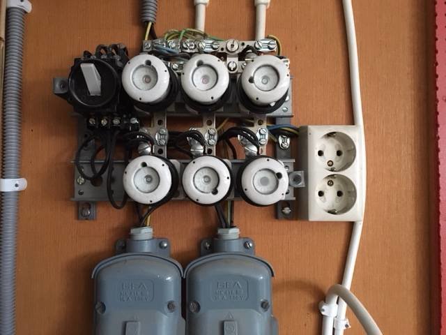 Gammal elcentral med tre svarta kablar, jord/nolla och äldre 380V uttag på vägg.