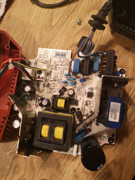Uppsprättad elektronisk apparat med synlig kretskort, transformatorer och kondensatorer, inga brännskador synliga.