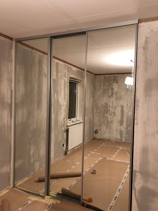 Renoveringsprojekt av sovrum med spegeldörrar, nakna väggar och golv skyddat med papper.