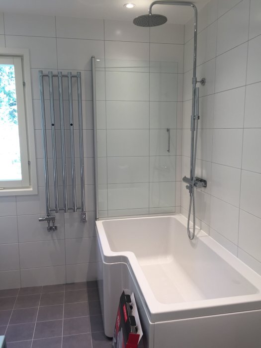Modernt badrum med vit badkar, infällbar duschvägg i klarglas och rostfri takdusch.