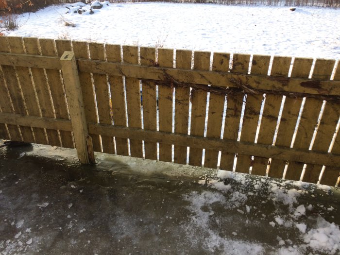 Trädäck med gammalt slitet trästaket med snö på marken i bakgrunden.