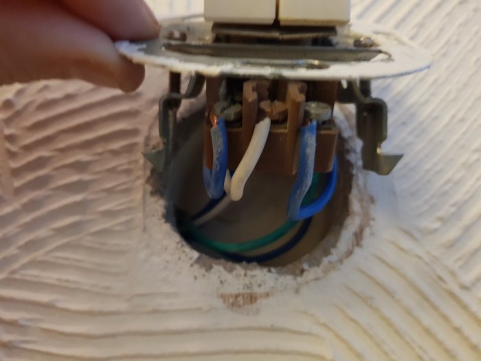 Hand som håller en urtagen eluttaget visar trådar och anslutningar bakom i en vägg under installation.