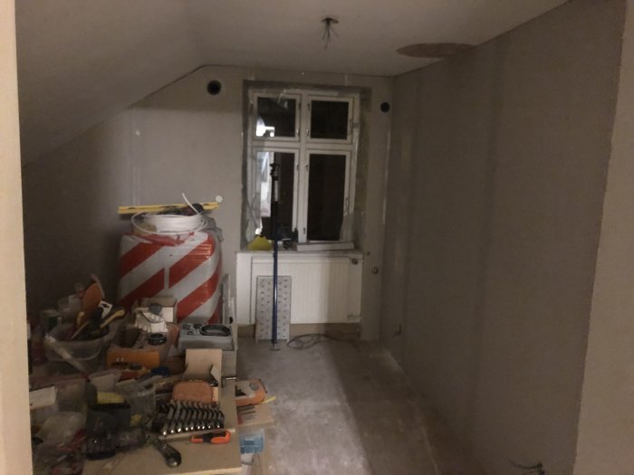 Ett rum under renovering med nyligen uppsatta gipsskivor på väggarna och rörig byggplats.