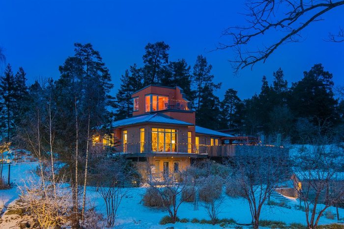 En modern villa upplyst i skymningen med snötäckt trädgård och omgivande skog.