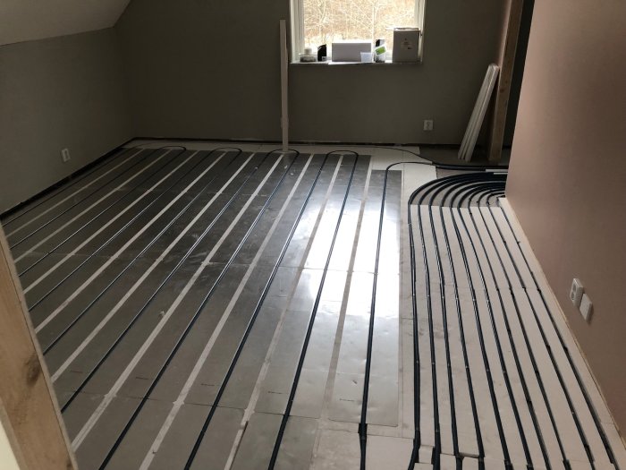 Installation av golvvärme med synliga rör och förbindningsskarvar i ett oinrett rum.