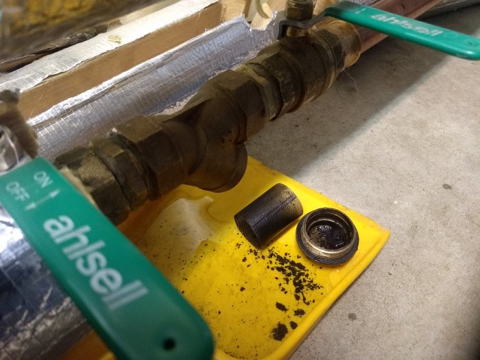 Rörgänga med på/av-spak och öppnat smutsfilter med borttaget lock och synliga smutspartiklar på gul bricka.