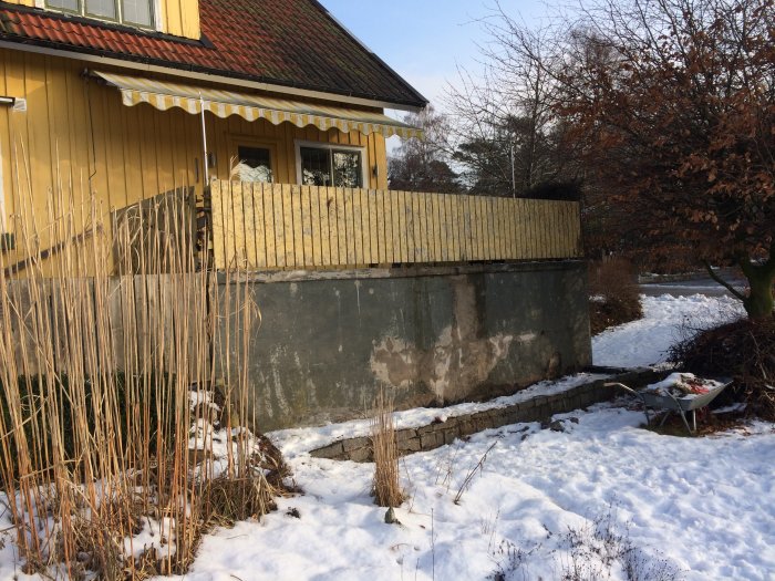 Altan med skadat staket och betongkonstruktion i dåligt skick ovanpå ett garage, omgivet av snö.