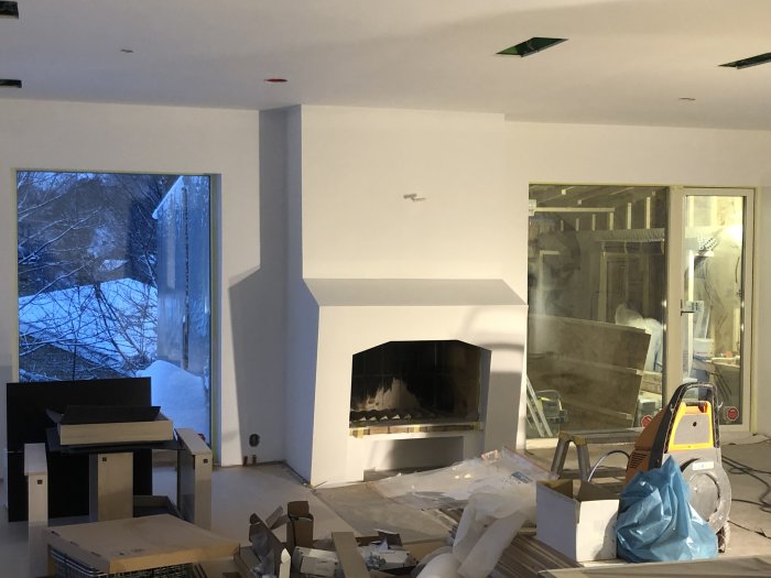 Renoveringsarbete inne med öppen spis, rörigt rum, byggmaterial och verktyg synliga.