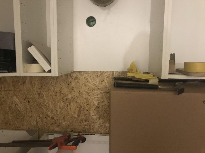 Plats för installation av köksfläkt utan täcksida under köksskåp, med verktyg och byggmaterial.