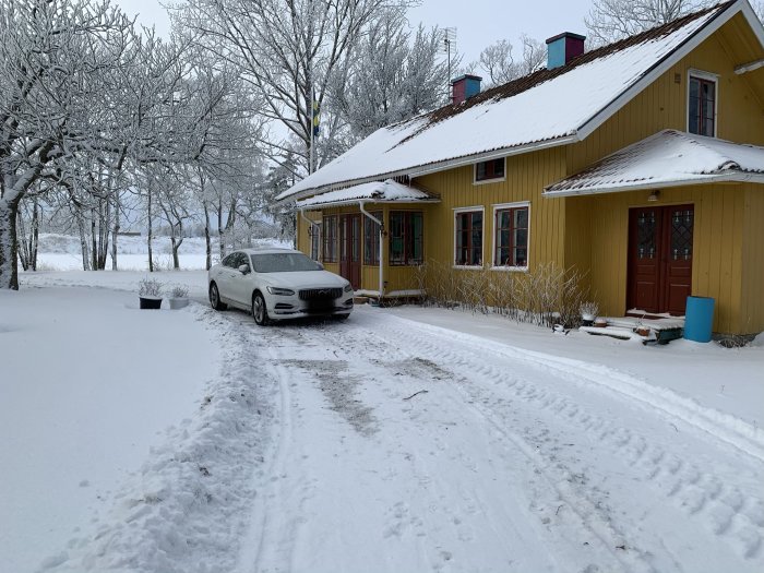 Gult hus med snö på taket och en bil parkerad framför i ett snötäckt landskap.