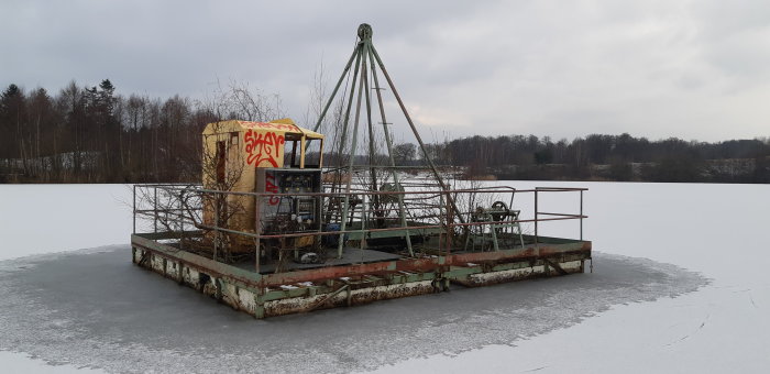 Övergiven plattform med graffiti på en frusen sjö omgiven av vinterlandskap i Skåne.