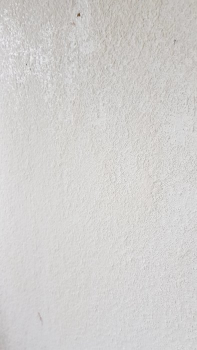 Vägg med ojämna rester av renoveringstapet och vitmålad underliggande spånskiva.