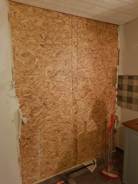 OSB-skiva uppsatt där kökskakel och gipsskiva tagits bort under renovering.