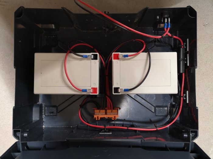 Batteri backup-system under konstruktion med två batterier och ledningar i en svart låda, 90% färdigställt.