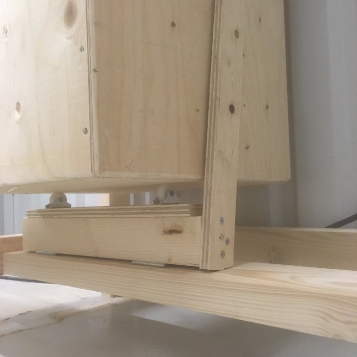 Träkonstruktion med sågspårslist mellan övre och nedre del, fästelement och skruvar synliga.