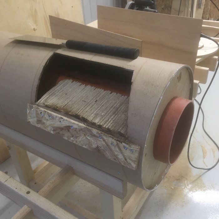 En halvfärdig spåntratt för en cyklon med fasat ändstycke och råsågade vinkelskärningar mot en verkstadsbakgrund.