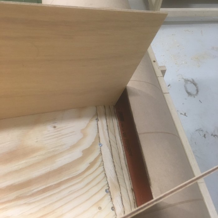 Pågående bygge av en cyklon spåntratt i trä med fasade kanter och skruvförband på ett byggarbetsbord.