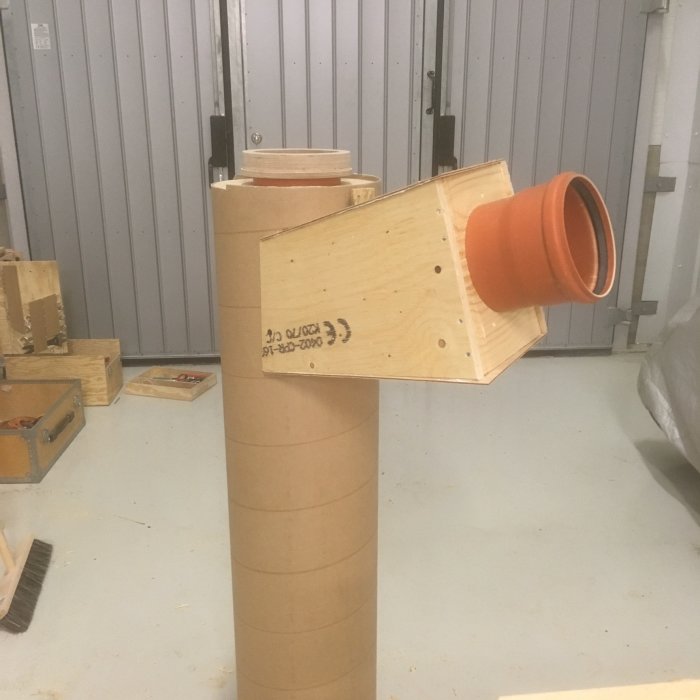 Hemmagjord spåntratt för cyklon med handsågade trädelar och en orange tratt monterad på toppen.