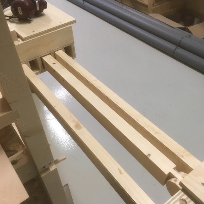 Utbyggda stödben på en sågbänk i ett verkstadsutrymme, med ställbara fötter och uppfällbart system.