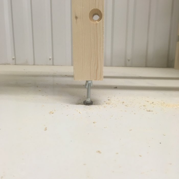 Utdragbart stödben för sågbänk med justerbar fot på ojämnt golv, träspån syns.