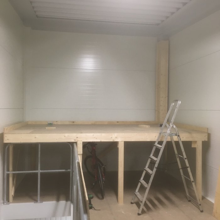 Nybyggt träloft i ett garage med stege, cykel och arbetsbänkar under konstruktion.