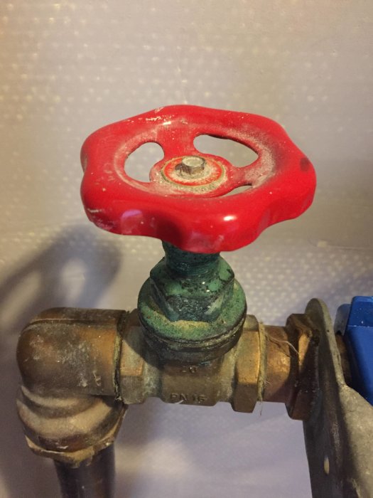 Röd ventilkon med läckage på undersidan mot en rörkoppling, möjliga tecken på korrosion och smuts.