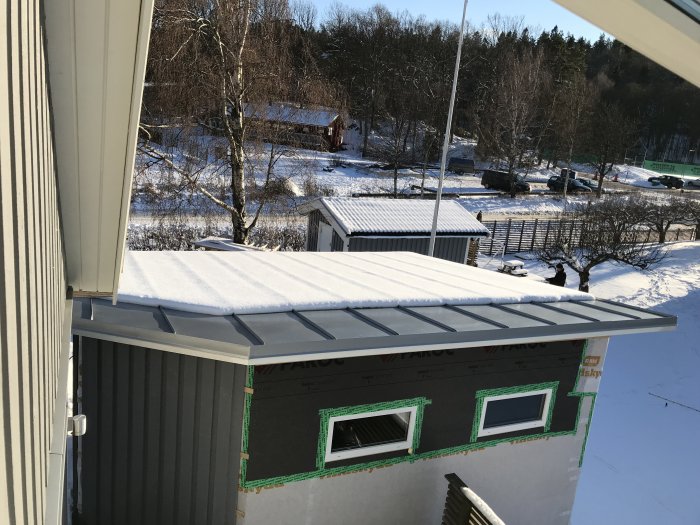 Snö på ett hus med flackt tak i soligt vinterlandskap som glider av på framsidan.