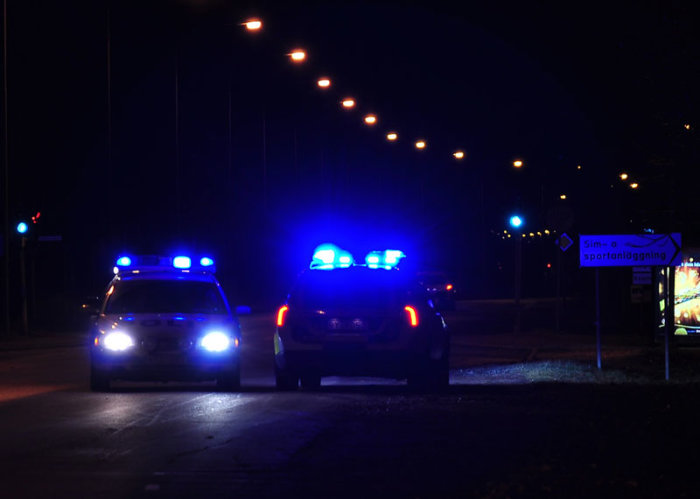 Två polisbilar med blåljus i mörkt stadsmiljö.