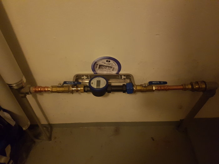 Väggmonterat vattenmätarsystem med nyinstallerad fjärrmodul och kopplingar för hushållsvatten.