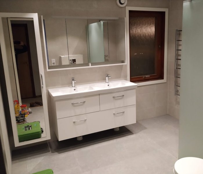 Renoverat badrum med dubbel tvättställ, spegelskåp, fristående badrumsskåp och handdukstork.