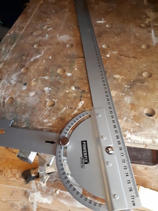 En vinkelhake från POWERFIX® på ett använd verktygsbord, vilket visar märkning av centimeter och grader.