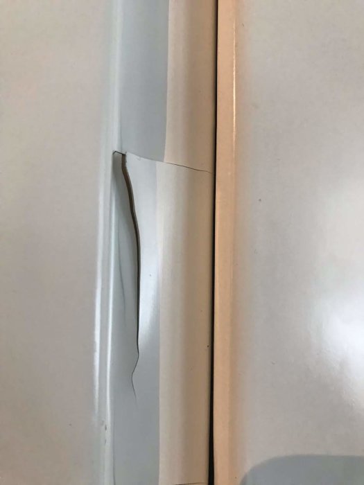 Närbild på vit kökslucka med flagnande färg och sprickor längs kanten.