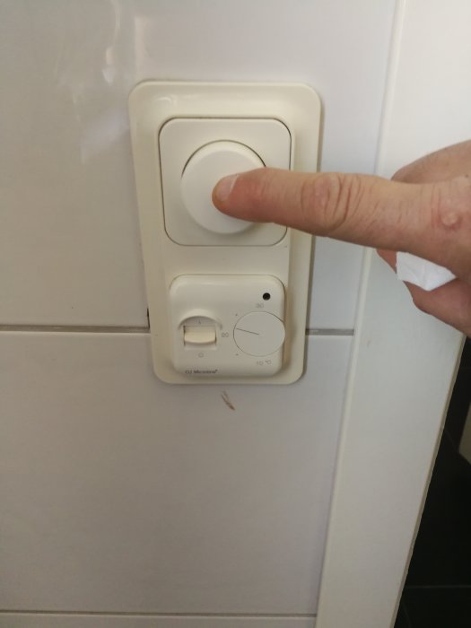 Hand trycker på en ELJO dimmerbrytare på en vägg.