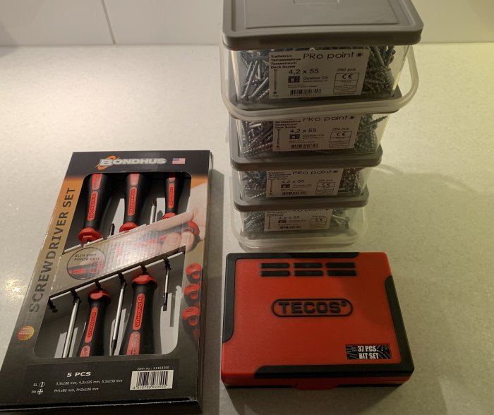 Nya skruvmejslar i förpackning, staplade lådor med trallskruv och en låda med bits.