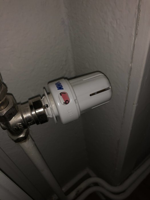Termostat monterad på en radiatorventil mot en vitvägg, inställd på mellanläge mellan rött och blått.