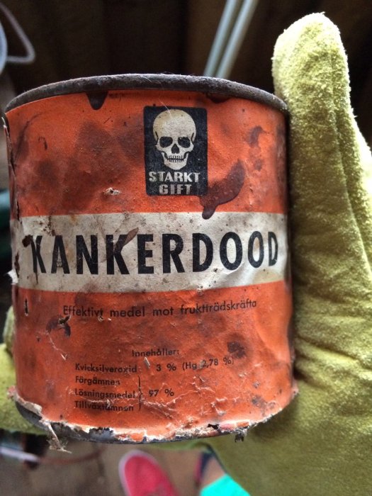 Hand håller en gammal skadad behållare med texten "KANKERDOOD", varningssymbolen för gift och ingredienslistan.