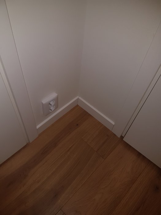 Renoverat hörn med trägolv och nyinstallerad eluttag mot vita väggar.
