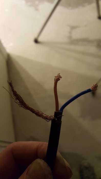 Hand håller en värmekabel med tre uppskalade slut: en blå, en brun och en oisolerad jordtråd.