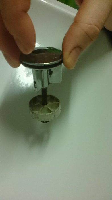 Närbild på en gammal handfatssil där silen och proppen är sammankopplade, med en persons fingrar som håller i proppen.
