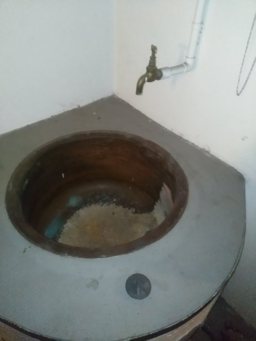 Gammal betongtvättbalja med träränna och vattenkran i ett hörn av en tvättstuga.