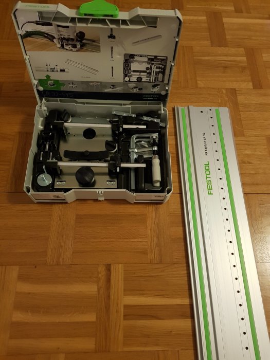 Verktygssats för gångjärn och expansionsbeslag i öppen låda bredvid en skena på ett trägolv.